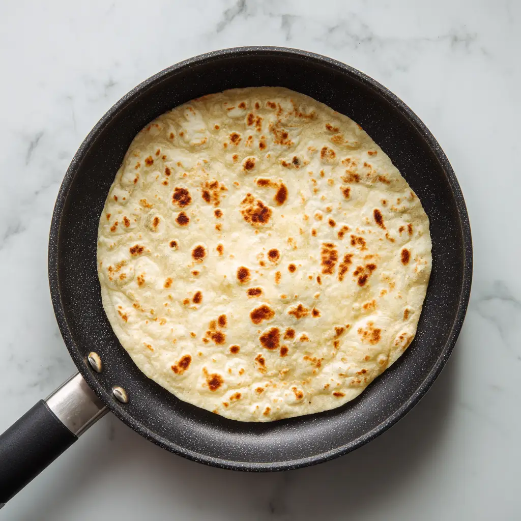 Grilled Chicken Caesar Wrap Step 2 — warm tortilla in plain skillet on white marble